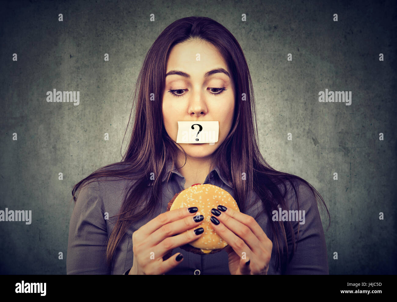 Frau auf Diät Beschränkung mit Fragezeichen auf den Mund leckere Burger auf grauem Hintergrund isoliert betrachten Stockfoto