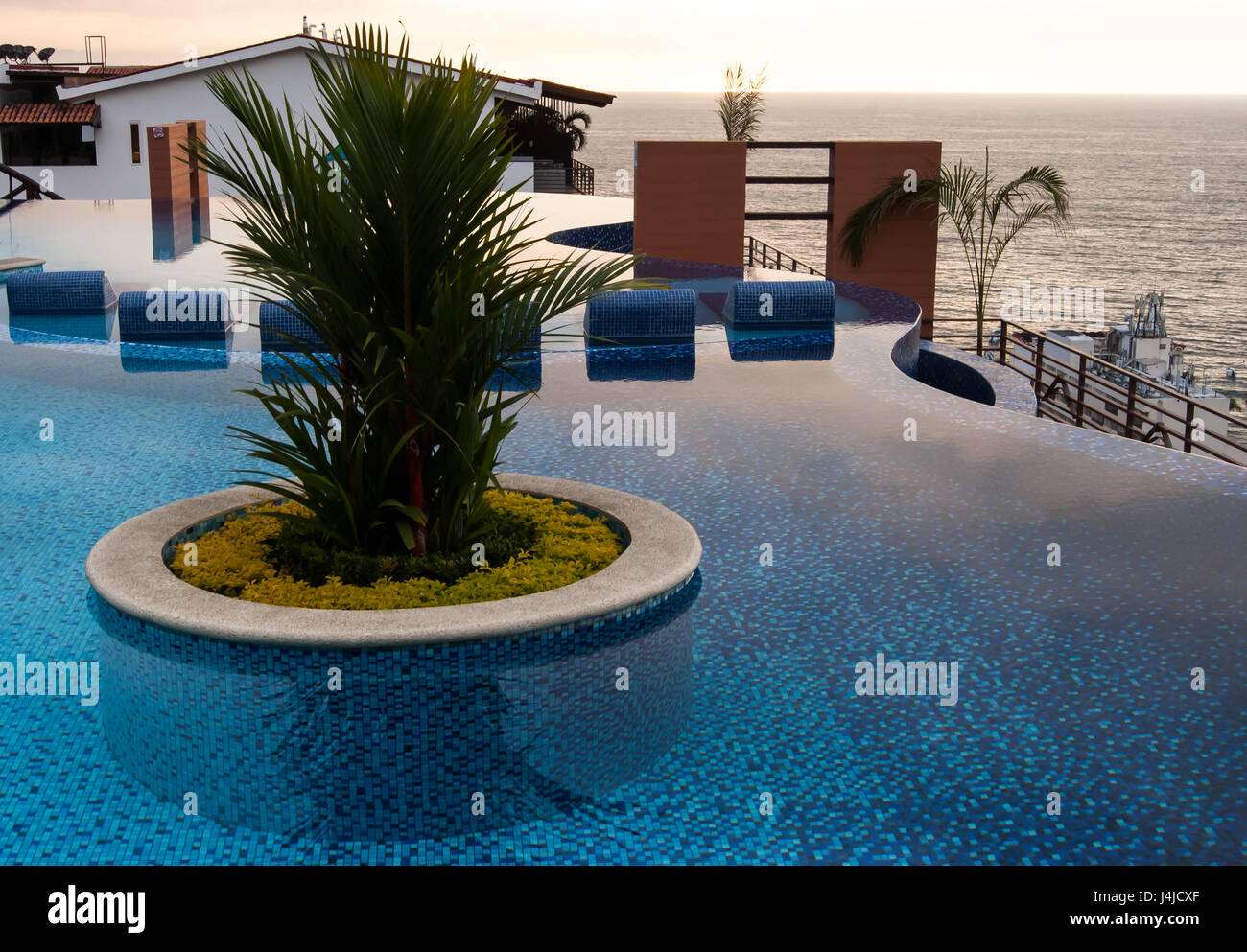 Ein Dach Swimmingpool mit schönen runden exotischen Pflanzer in der Mitte und am Abend/Nacht Blick auf Meer und Stadt Stockfoto