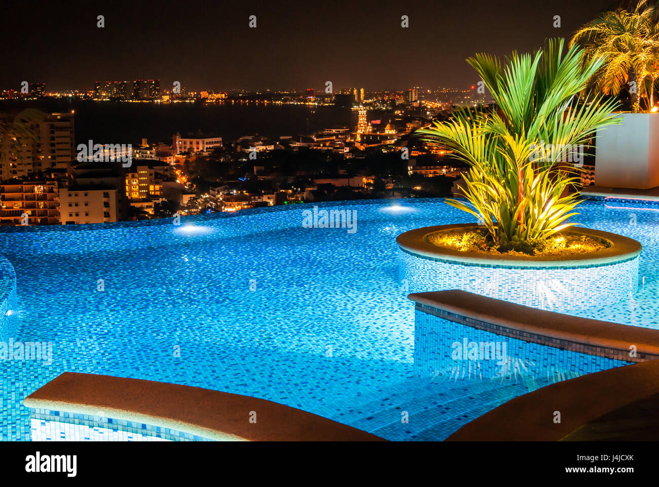 Ein Dach Swimmingpool mit schönen runden exotischen Pflanzer in der Mitte und am Abend/Nacht Blick auf Meer und Stadt Stockfoto