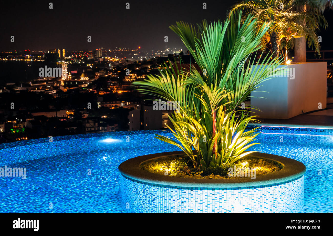 Ein Dach Swimmingpool mit schönen runden exotischen Pflanzer in der Mitte und am Abend/Nacht Blick auf Meer und Stadt Stockfoto