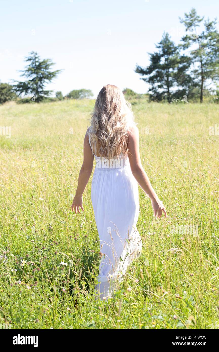 Junge Frau in langen weißen Kleid wandern in der Wiese. Stockfoto