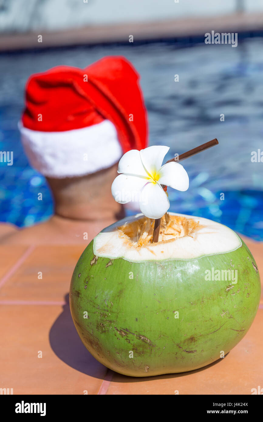 Kokosnuss Saft trinken mit Mann in Weihnachten Weihnachtsmütze am Pool - tropischen Ferienkonzept Stockfoto