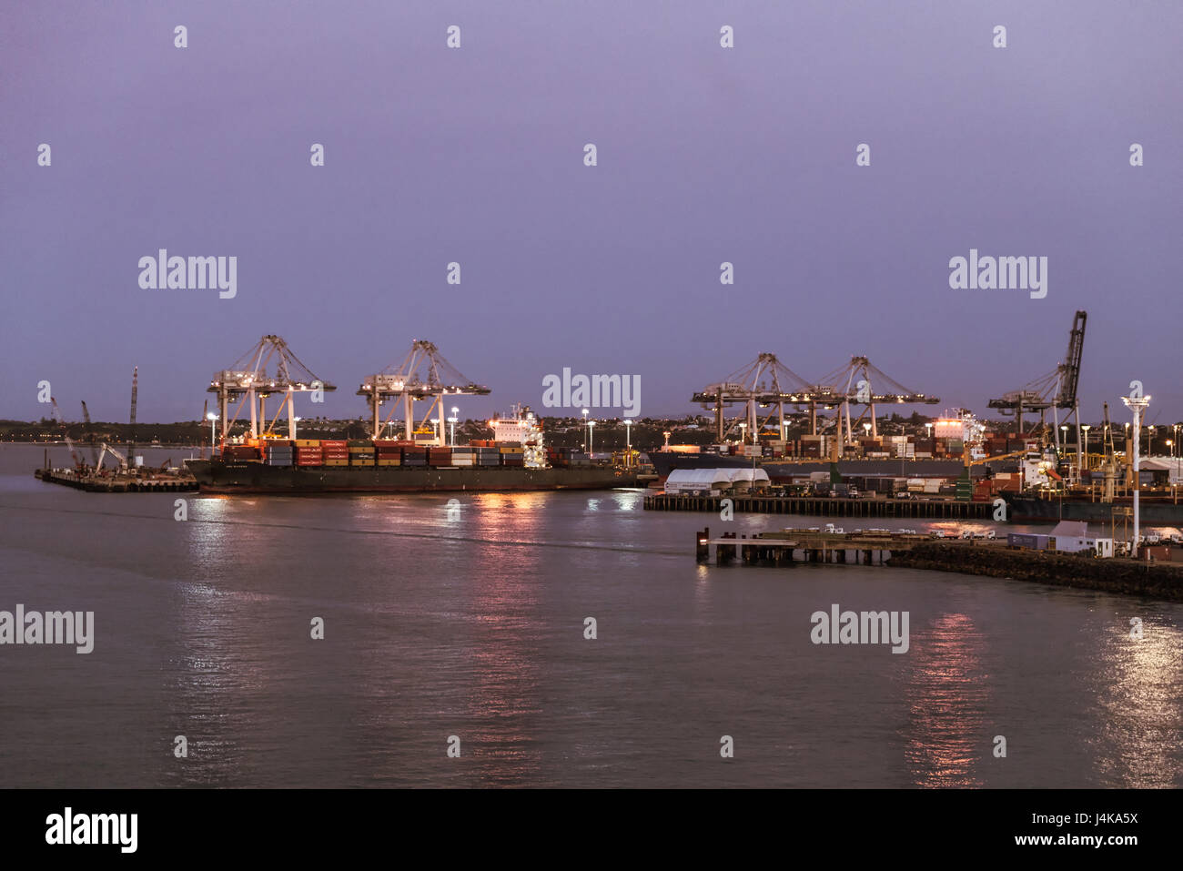 Auckland, Neuseeland - 6. März 2017: Übersicht des Containerterminals bei Sonnenuntergang mit Schiffen. Lichter auf den Docks im Wasser gespiegelt. Stockfoto