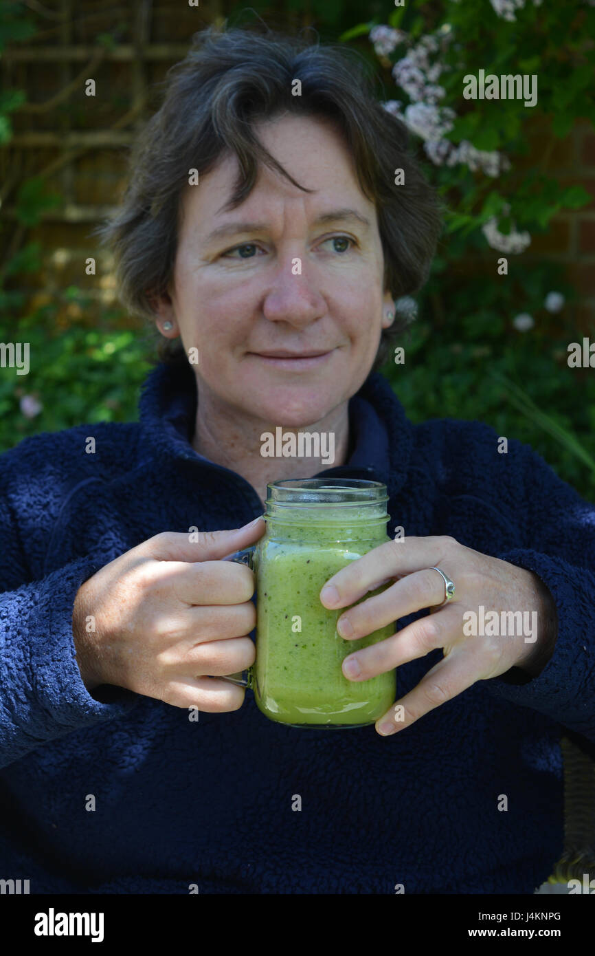 Frau hält einen grünen Gemüsen Smoothie, sitzen im Freien. Stockfoto