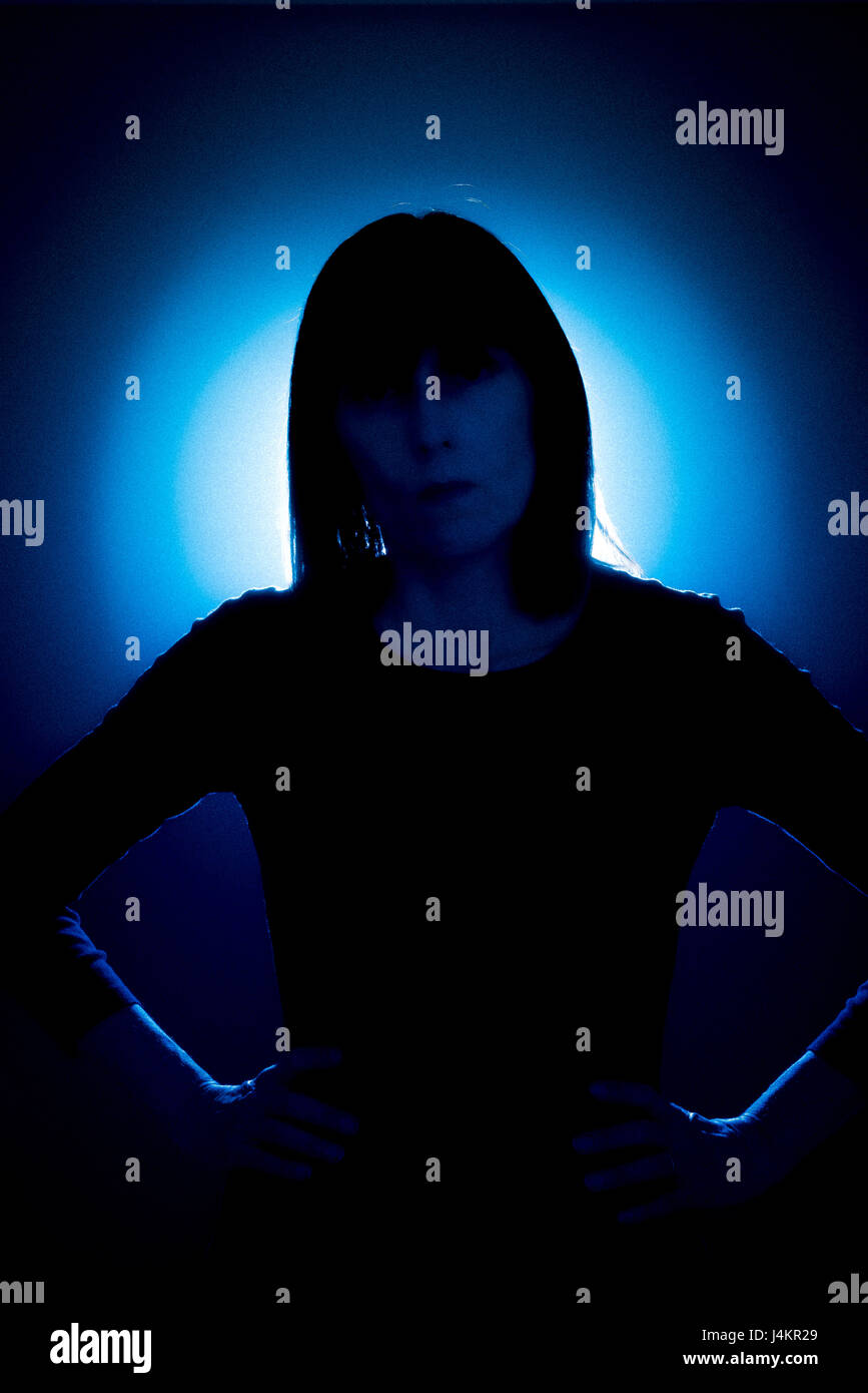 Silhouette des weiblichen gerichtete Kamera mit Händen auf den Hüften gegen blauen Fleck ausgeleuchteten Hintergrund Stockfoto