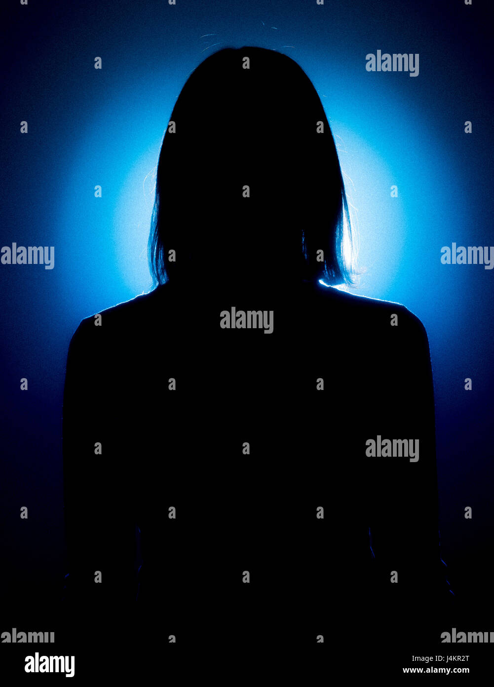 Silhouette des weiblichen mit Rücken zur Kamera vor blauen Fleck beleuchteten Hintergrund Stockfoto