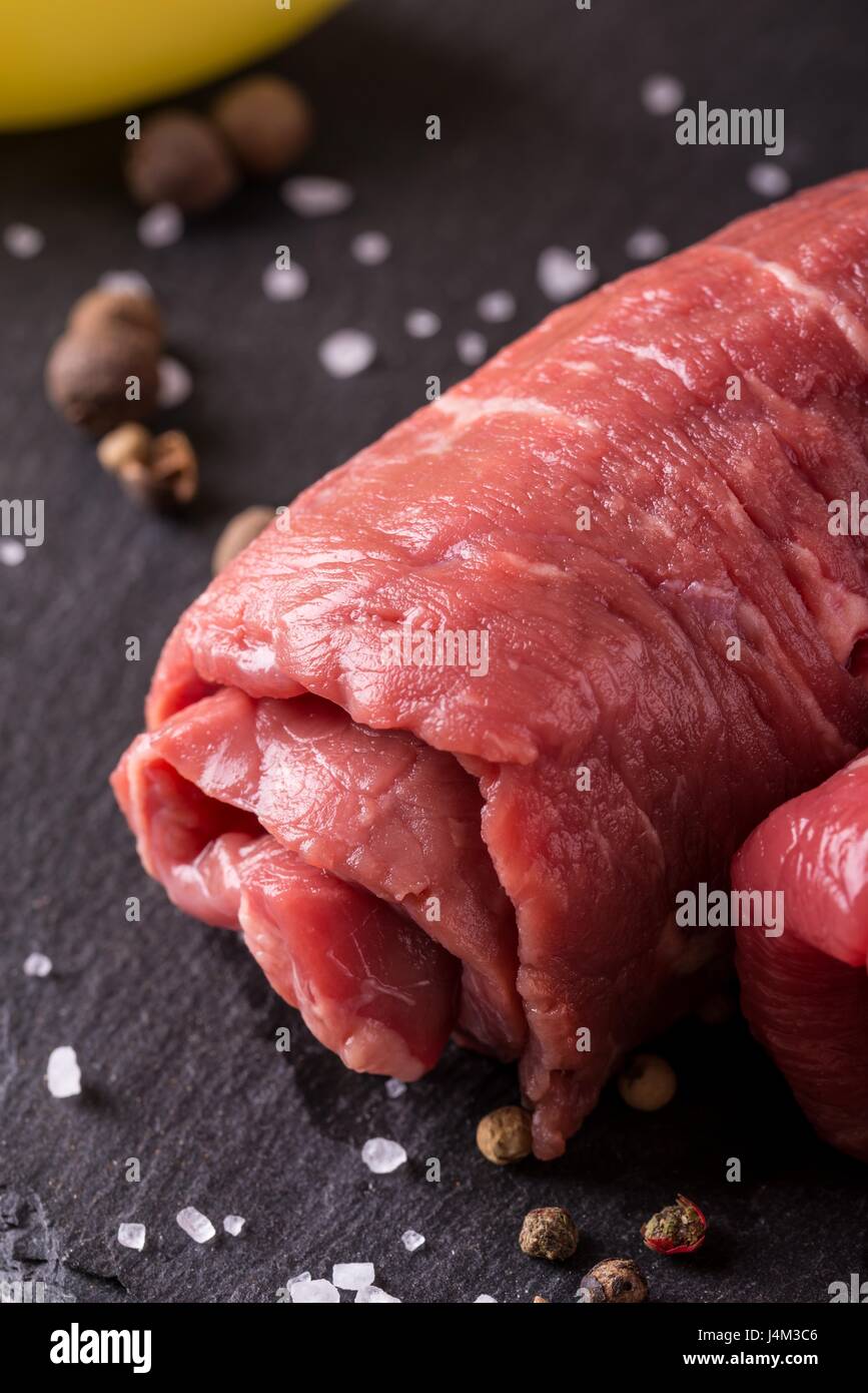 Vertikale Foto mit Details der einzelnen gewalzten Rindfleisch Slice. Fleisch für die Roulade vorbereitet und auf schwarzem Schiefer mit mehreren Gewürzen verschüttete Aroun platziert Stockfoto