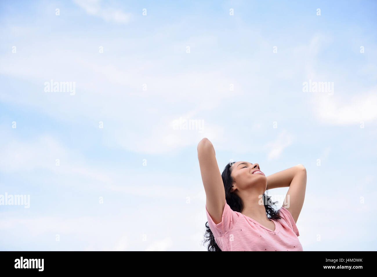 Hispanic Frau mit Händen im Haar unter bewölktem Himmel Stockfoto