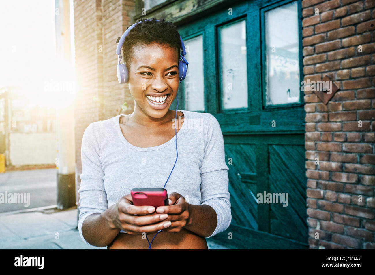 Lächelnde schwarze Frau anhören Handy mit Kopfhörern in Stadt Stockfoto