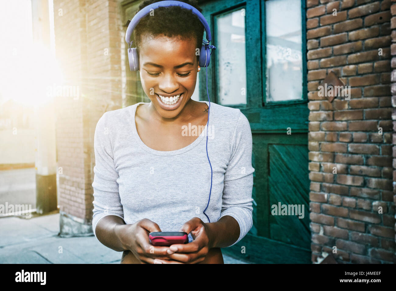 Lächelnde schwarze Frau anhören Handy mit Kopfhörern in Stadt Stockfoto