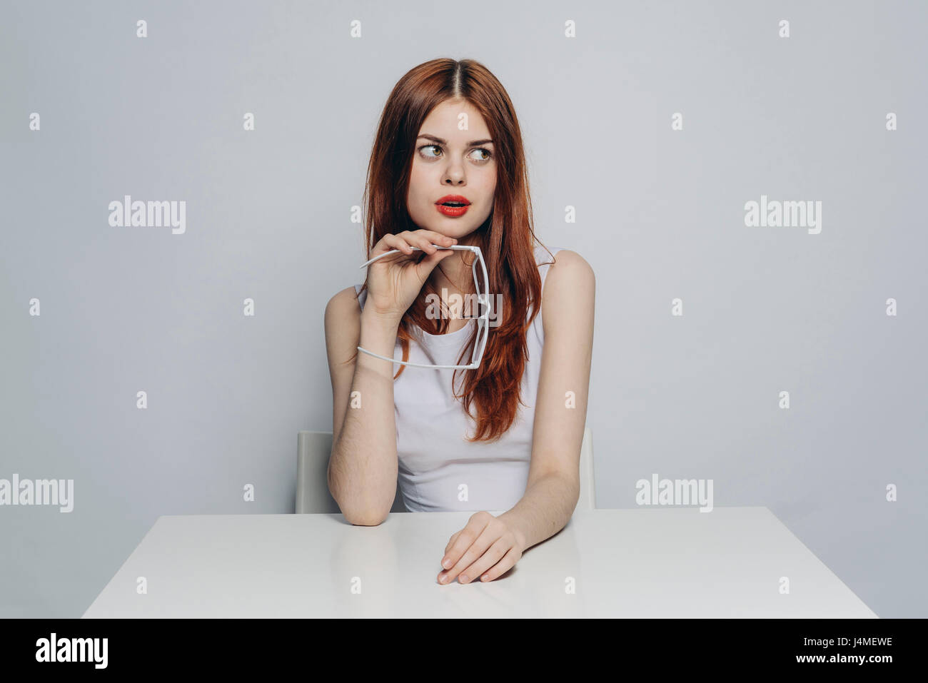 Neugierig kaukasischen Frau sitzt am Tisch halten weiße Brille Stockfoto