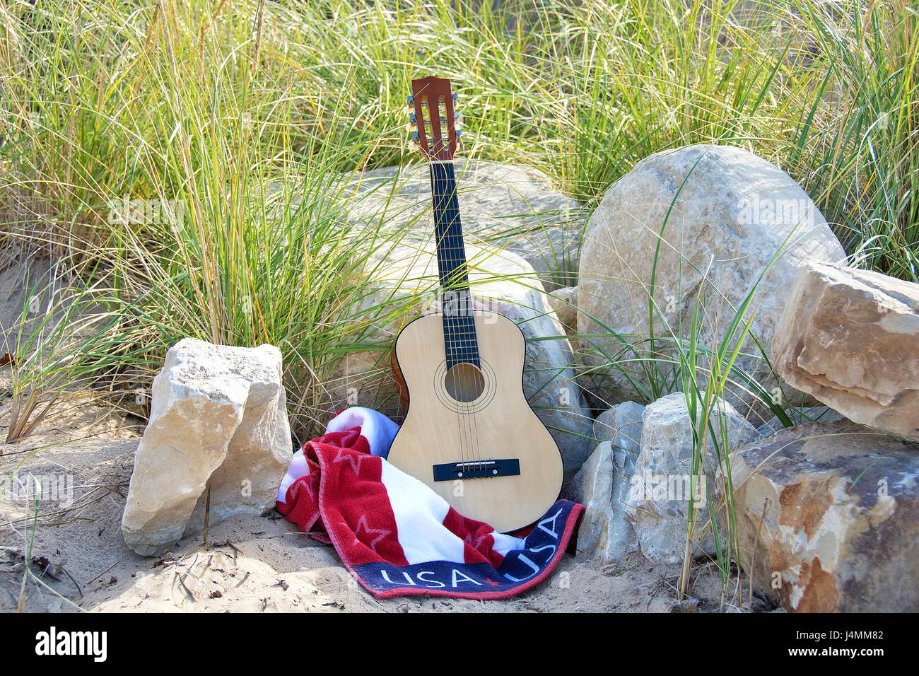 sechs string Gitarre auf USA Flagge Handtuch am Strandsand mit Felsen Stockfoto