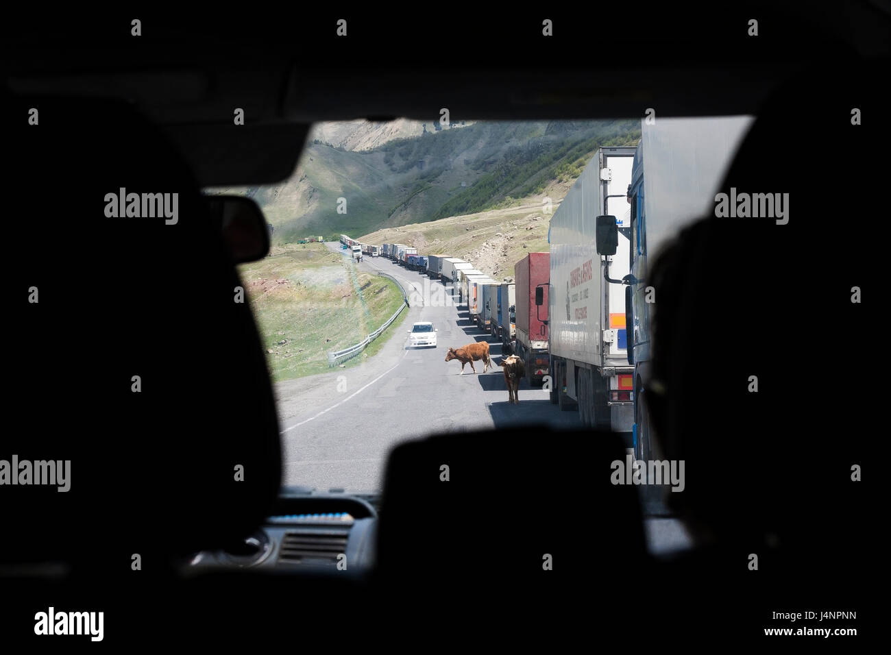 Ein Blick durch die Windschutzscheibe eines Busses aus einer langen Reihe von Lastwagen, die darauf warten, in Russland Ende der militärischen Autobahn, Kasbegi, Georgien zu überqueren Stockfoto