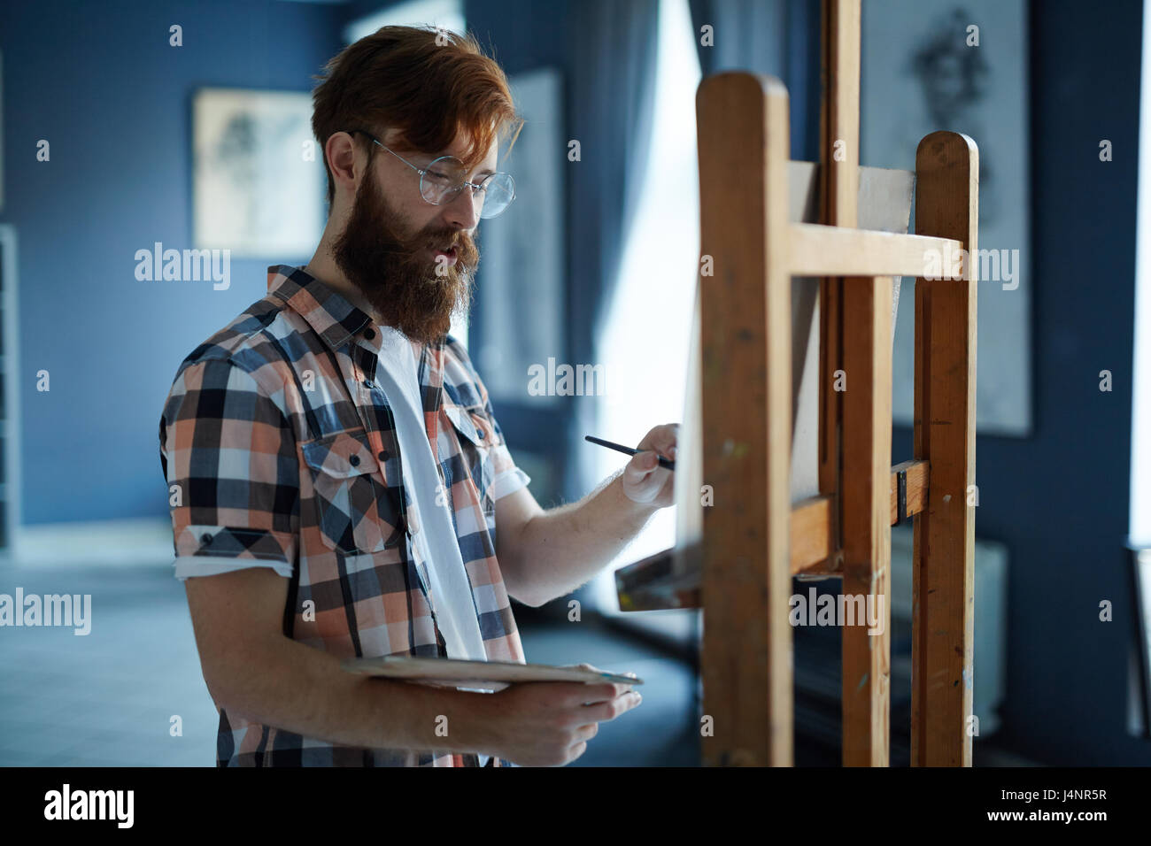 Porträt von fokussierten zeitgenössischer Künstler, Rothaarigen Mann mit Bart, Brille, Bild auf Leinwand im Atelier Stockfoto