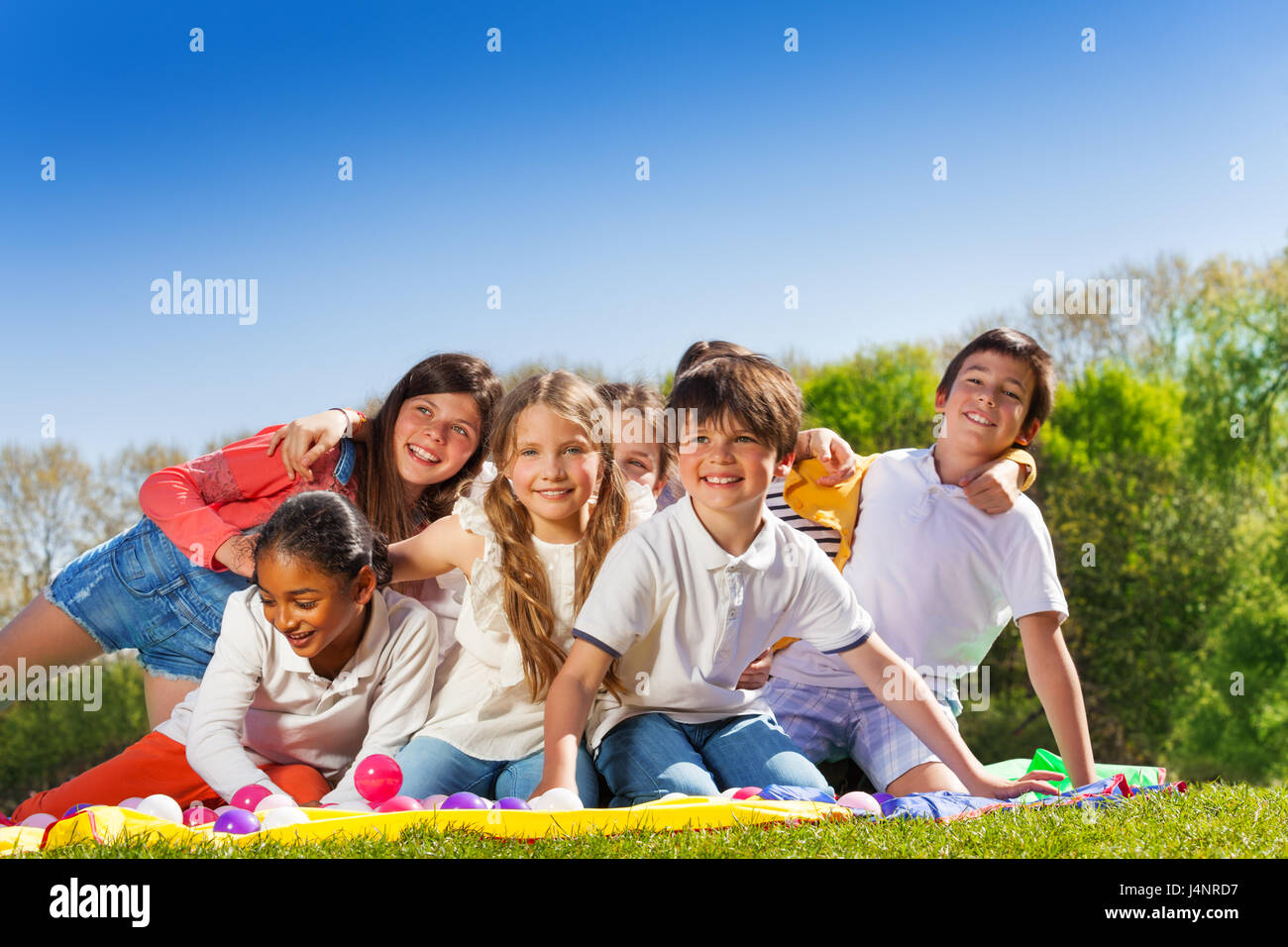 Große Gruppe von glückliche 10-12 Jahre alte Kinder, sitzen auf dem Rasen im Park, umarmen und lachen Stockfoto