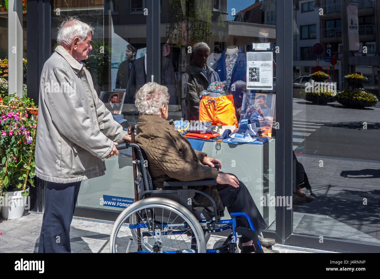 Pensionierter Mann mit behinderten älteren Frau im Rollstuhl betrachten Schaufenster in Einkaufsstraße Stockfoto