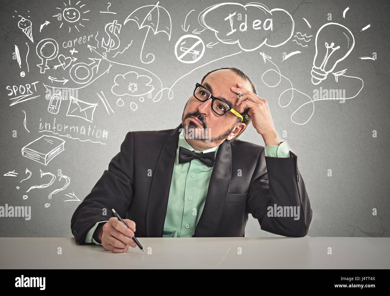 Nachdenklicher Mann am Tisch kratzte sich am Kopf denken, etwas zu schreiben bereit isoliert Büro graue Wand Background. Menschliches Gesicht Ausdruck emot Stockfoto