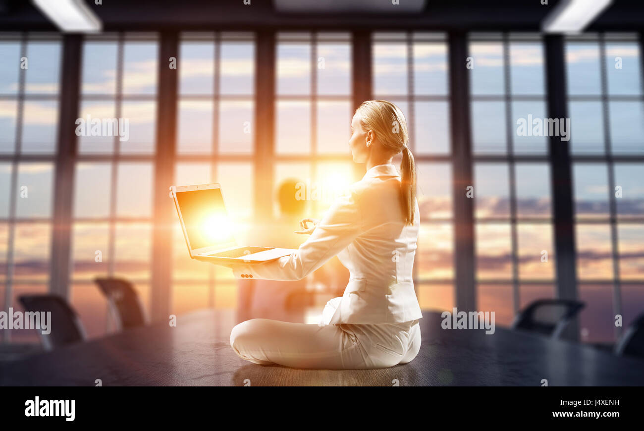 Junge attraktive Frau cross legged Lotus Yoga-Pose am Schreibtisch sitzen. Mixed-media Stockfoto