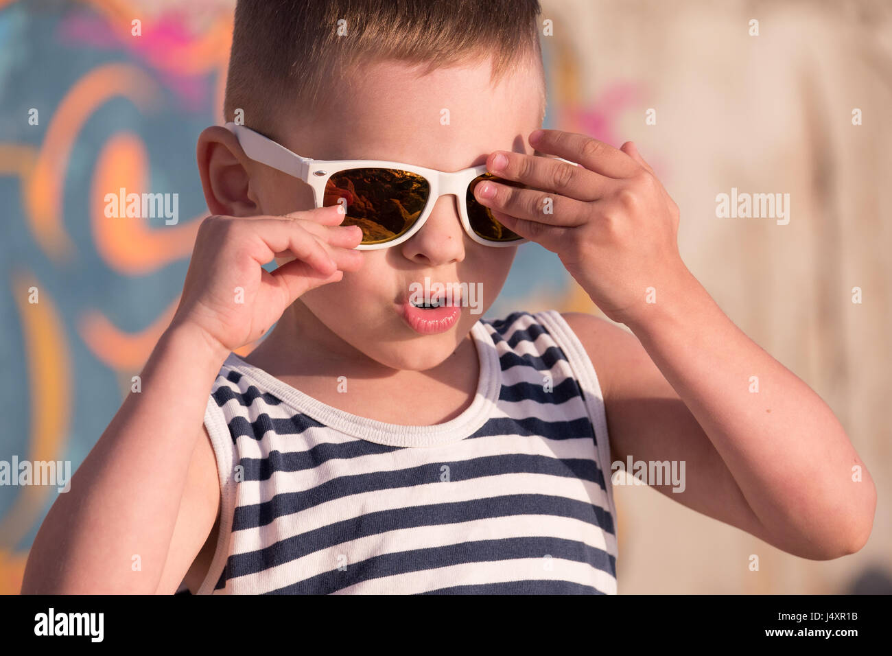 Schöne kleine junge weiße Sonnenbrille mit Sailor Streifen Weste auf Graffiti-Wand-Hintergrund berühren seine Sonnenbrille Stockfoto