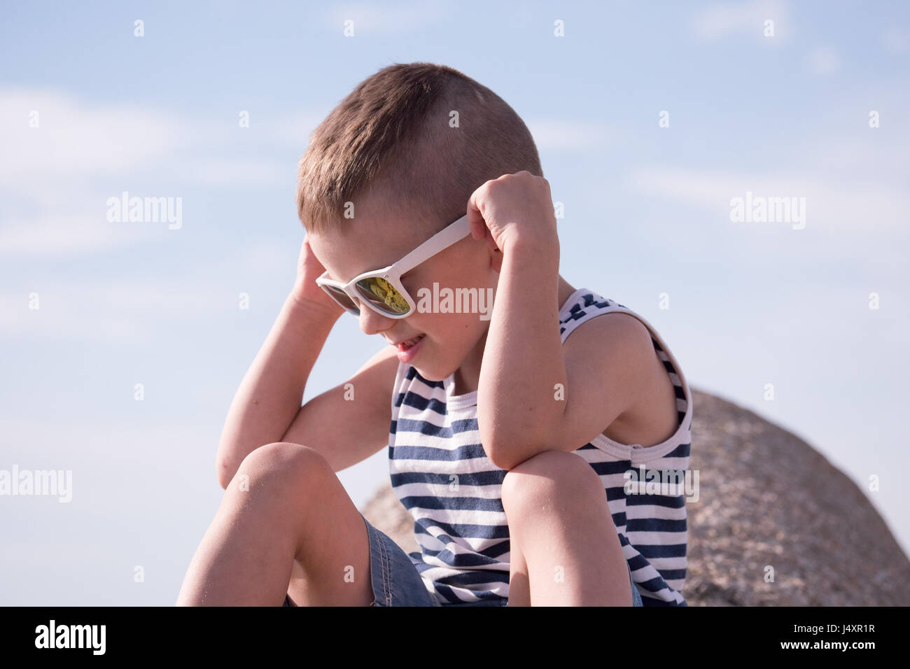 niedlichen kleinen Jungen tragen weiße Sonnenbrille und Sailor Streifen Shirt sitzen Stockfoto