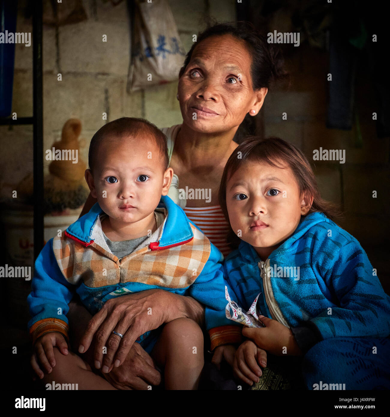 Eine Großmutter sitzt mit zwei ihrer Enkelkinder in der Demokratischen Volksrepublik Laos. Sie ist auf einem Auge blind aus, etwas in ihr Auge gelangen, während die Landwirtschaft Reis Stockfoto