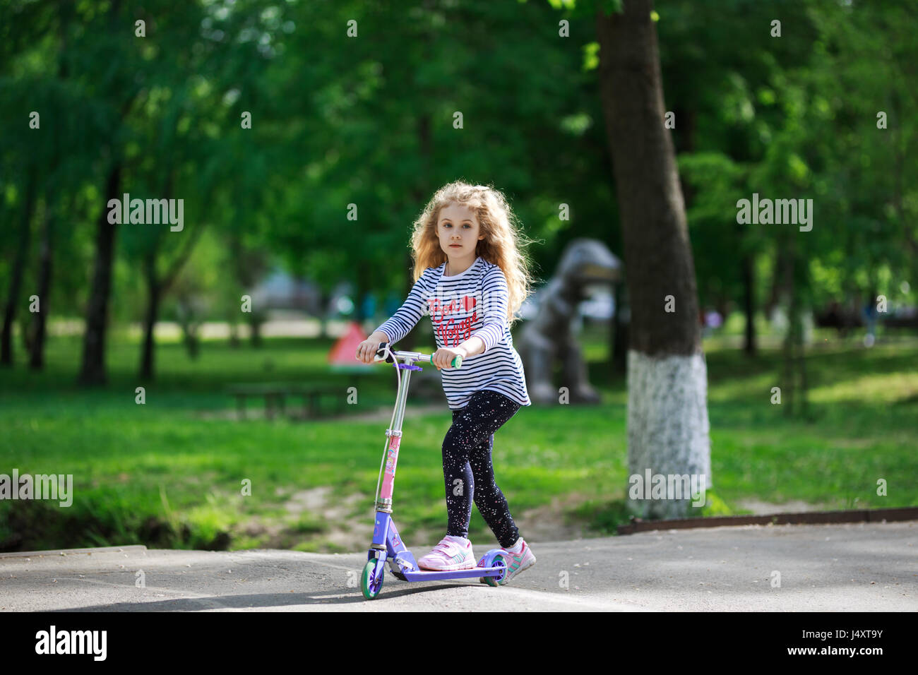 Kleine blonde Mädchen fahren die Roller in den Park. Stockfoto
