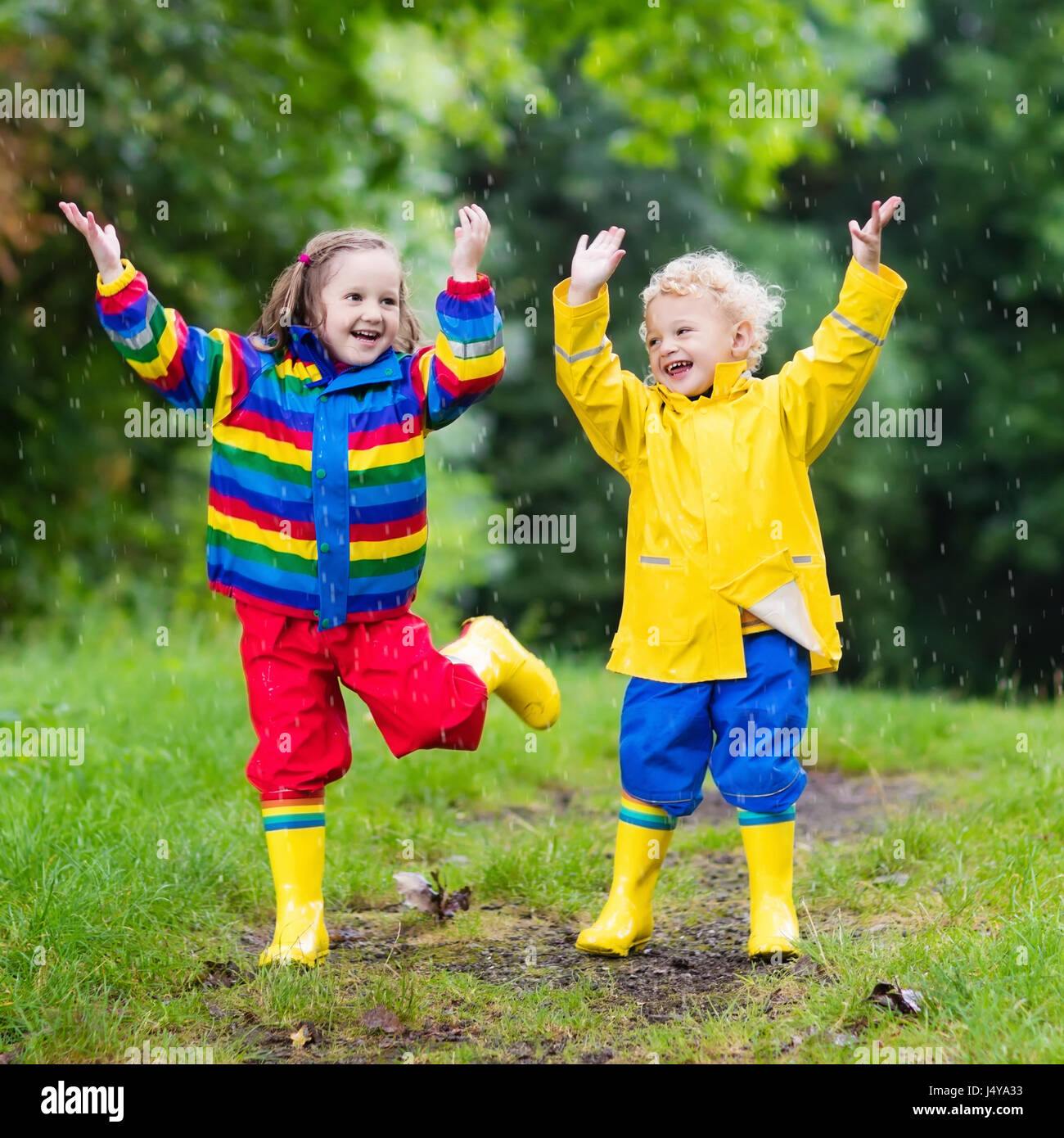 Kleine Jungen und Mädchen spielen im Regensommer Park. Kinder mit bunten Regenbogen  Jacke und wasserdichte Stiefel in Pfütze springen und Schlamm im Regen.  Kinder-wal Stockfotografie - Alamy