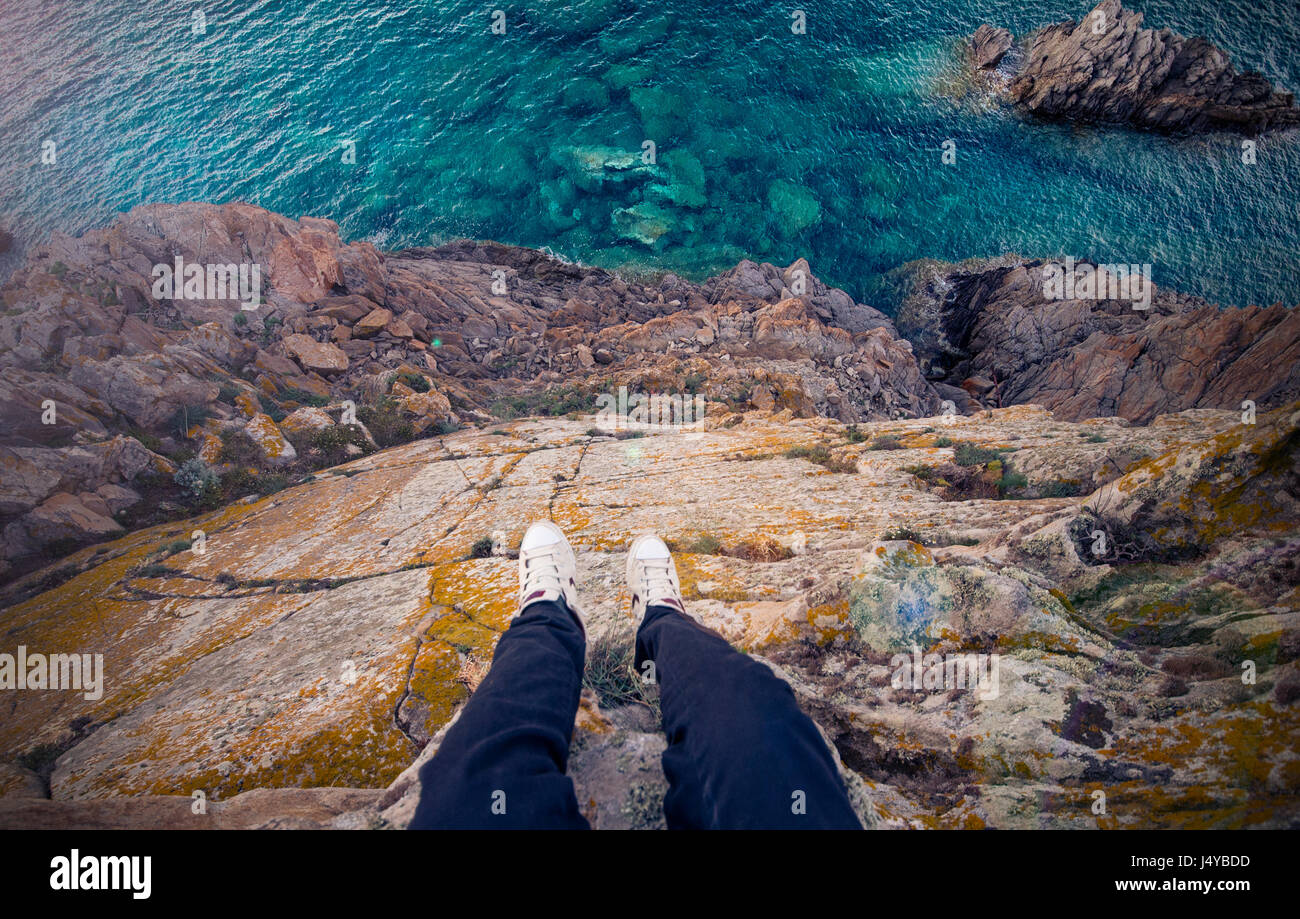 Ein Mann steht auf einem hohen Felsen von einer italienischen Küste mit dem Mittelmeer unter ihm. Porto Cervo - Costa Smeralda, Sardinien - Italien Stockfoto