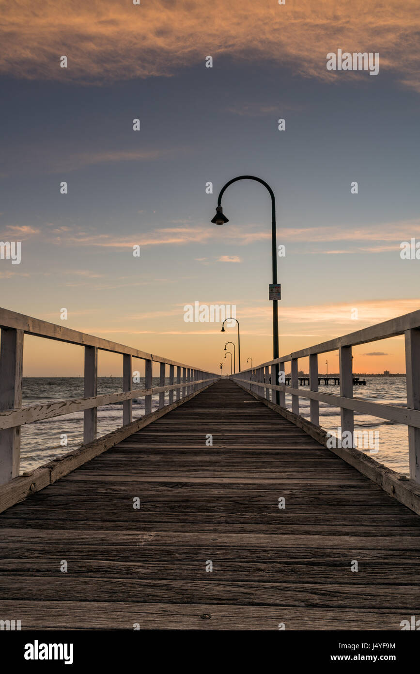 Ein Pier in Port Melbourne, Melbourne, Victoria, Australia.The Pier Geländer führen die Augen bis zum Horizont mit einem Sonnenuntergang geben eine Orange/goldene Farbton Stockfoto