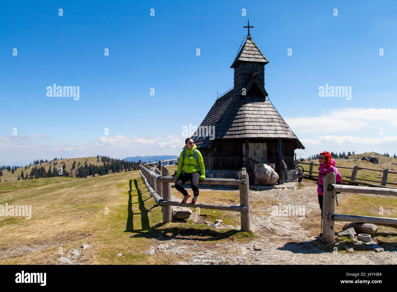 Glücklich lächelnd Wanderer ruht in der Nähe von kleinen Bergkirche in Bergnatur auf sonnigen Tag, Velika Planina, Slowenien gegen strahlend blauen Himmel Stockfoto