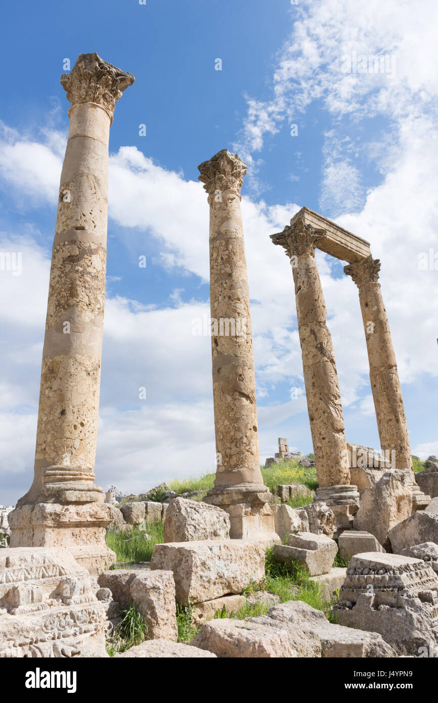 Antike römischen Säulen mit kunstvoll geschnitzt Hauptstädte und einen Stein Strahl mitten in Schutt und Asche in Jerash Jordanien. Blauer Himmel mit Wolken. Stockfoto