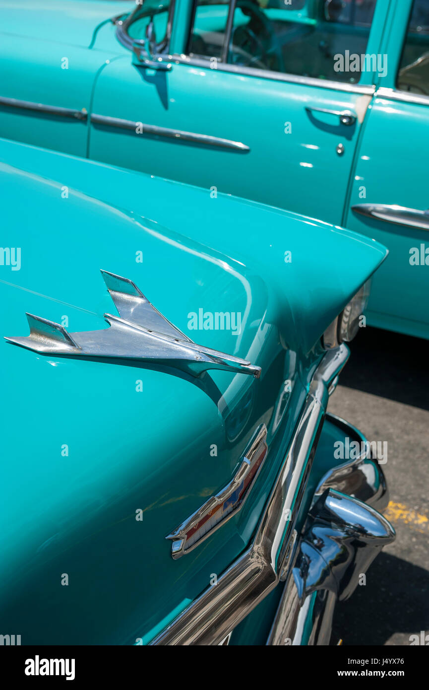 Havanna - ca. Juni 2011: Die Kühlerfigur von 1953 Chevrolet BelAir schimmert in der tropischen Sonne neben einem anderen amerikanischen Oldtimer in blauen Farbtönen. Stockfoto