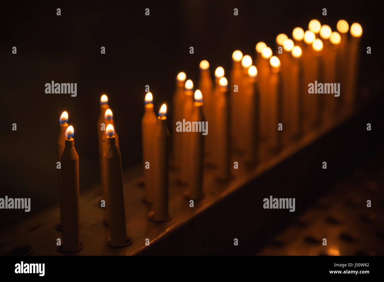 Brennende Gebet Kerzen stehen in einer Reihe, dunklen Innenraum der katholischen Kirche Stockfoto
