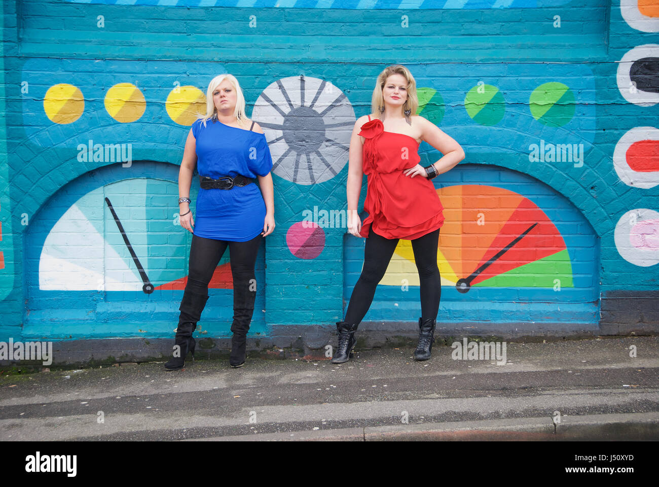 Zwei hübsche Mädchen vor einer Mulri-farbig bemalte Wand in rot und blau outfits Stockfoto