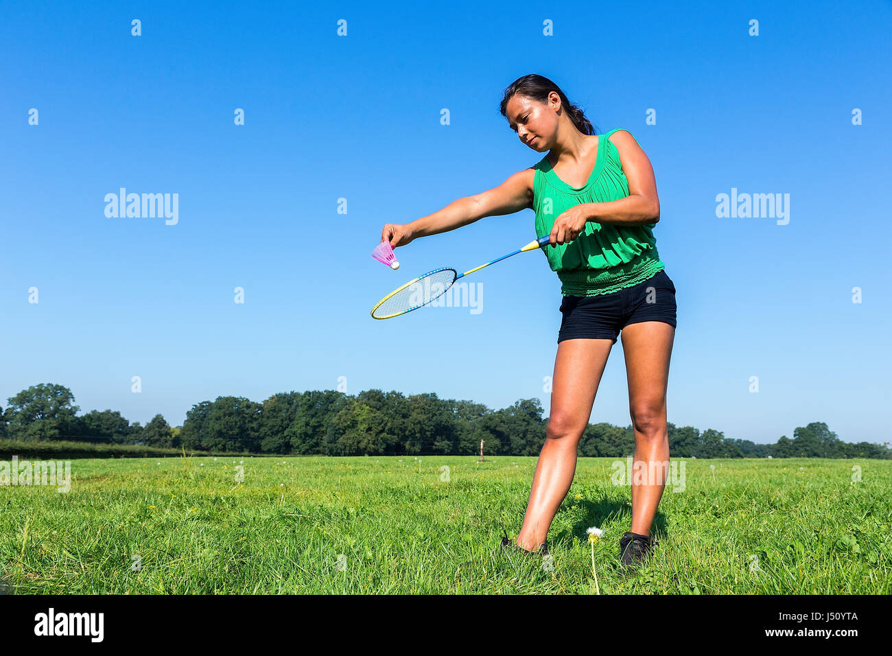 Kolumbianische Frau dienen mit Badminton-Schläger und Shuttle außerhalb Gras Stockfoto
