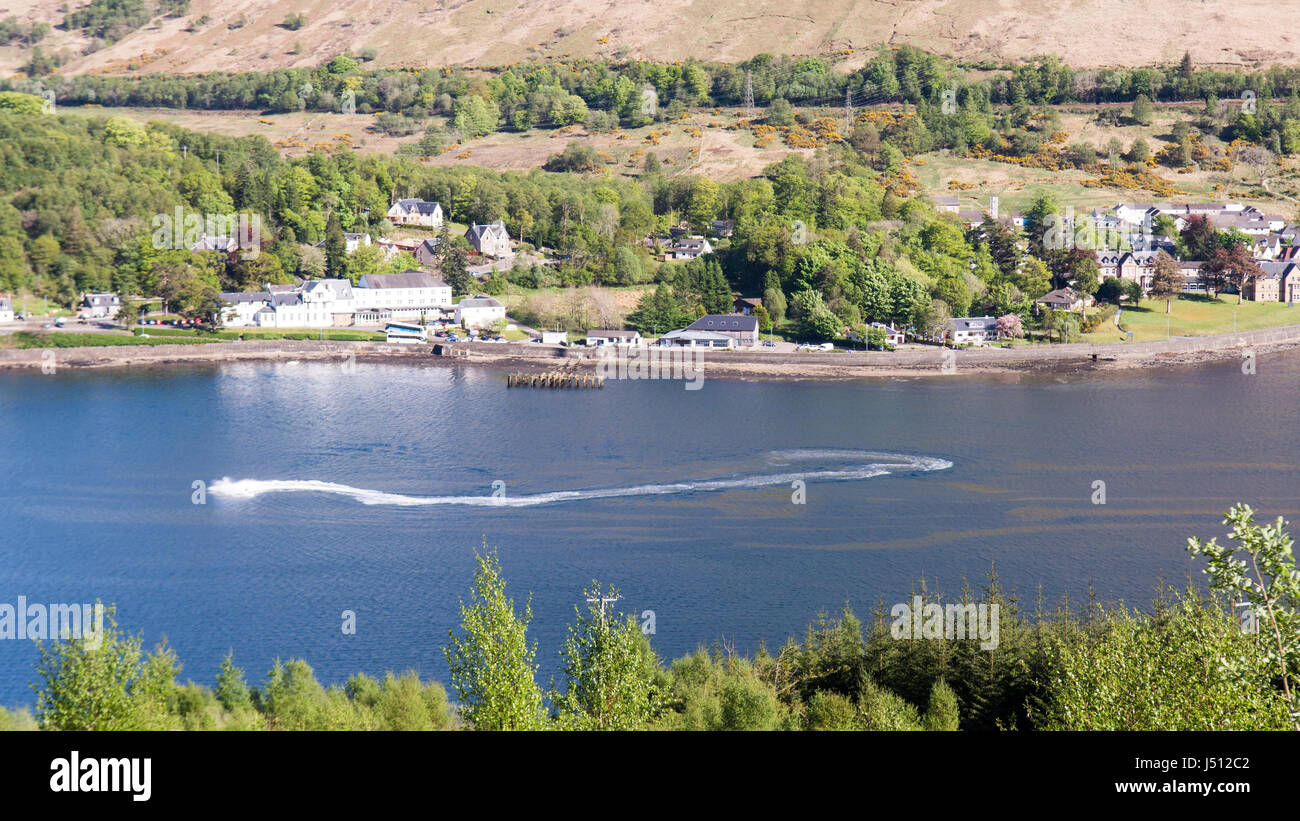 Ein Speed-Boot macht Wellen in Loch Long, ein Meer-See in den westlichen Highlands von Schottland, mit Arrochar Dorf hinter. Stockfoto