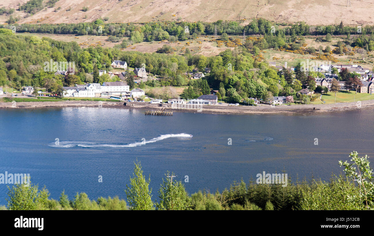 Ein Speed-Boot macht Wellen in Loch Long, ein Meer-See in den westlichen Highlands von Schottland, mit Arrochar Dorf hinter. Stockfoto