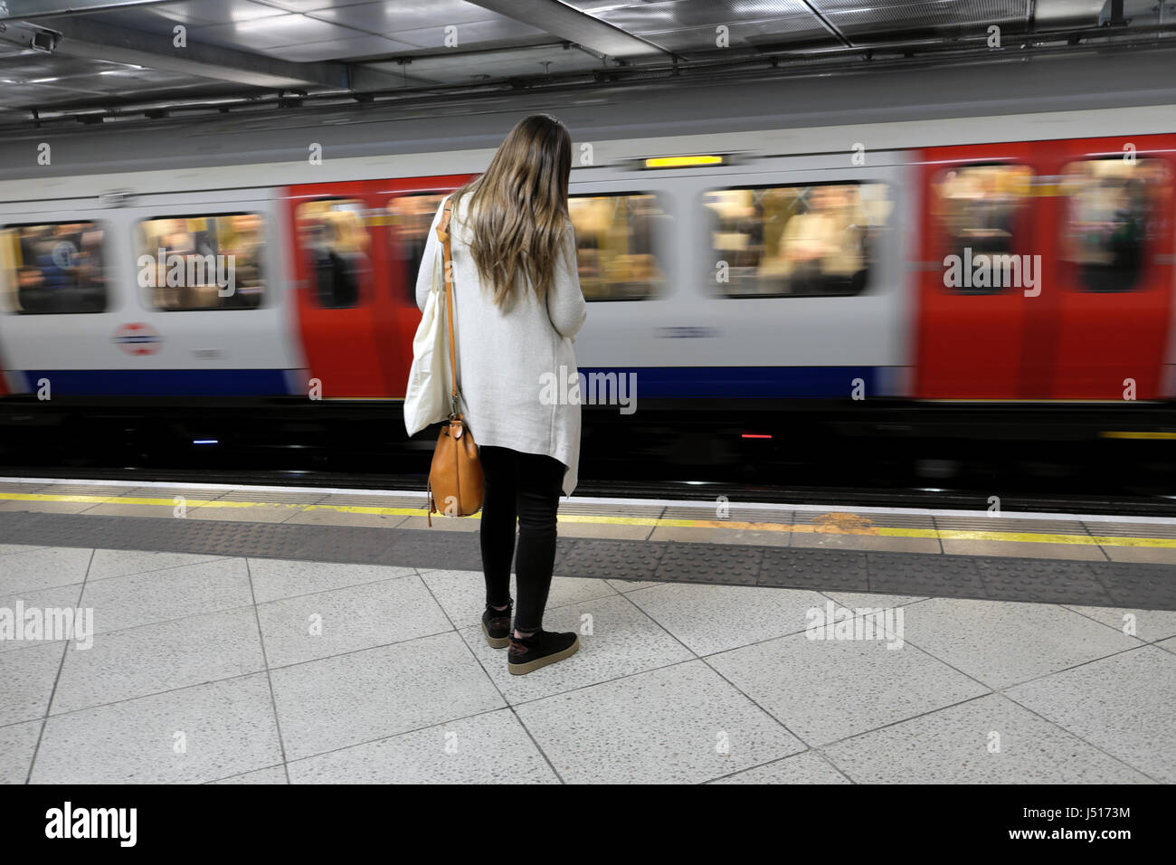Zurück Blick auf eine junge Frau, die am U-Bahnsteig mit dem Schnellfahren Zug passiert auf der anderen Seite der Spur in London UK KATHY DEWITT Stockfoto