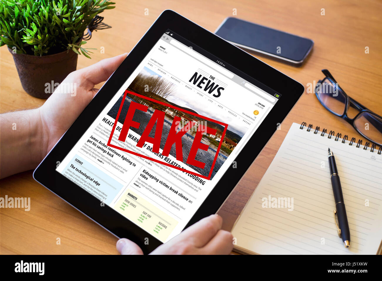 Hände eines Mannes Haltevorrichtung eine gefälschte Nachrichten über eine hölzerne Workspace-Tabelle. Alle Bildschirm-Grafiken bestehen. Stockfoto