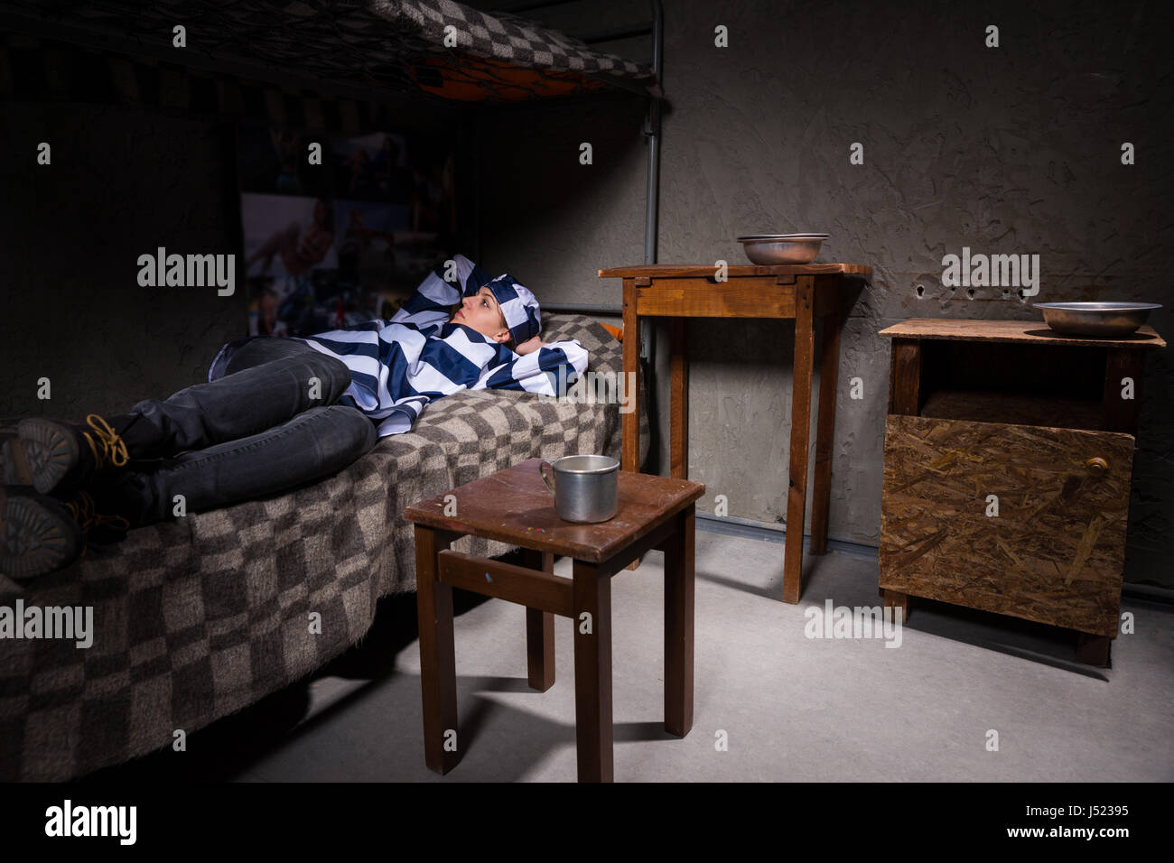 Junge Frau gefangen in Gefängnis Uniform hat in Gedanken beim liegen im  Bett in der Nähe von Nachttisch mit Aluminium-Gerichten in einer  Gefängniszelle verloren Stockfotografie - Alamy