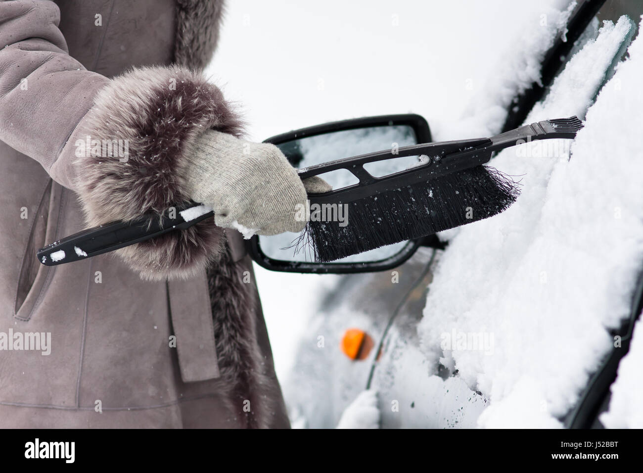 Hand der Frau im Handschuh ein Auto aus dem Schnee mit einer Bürste reinigen Stockfoto