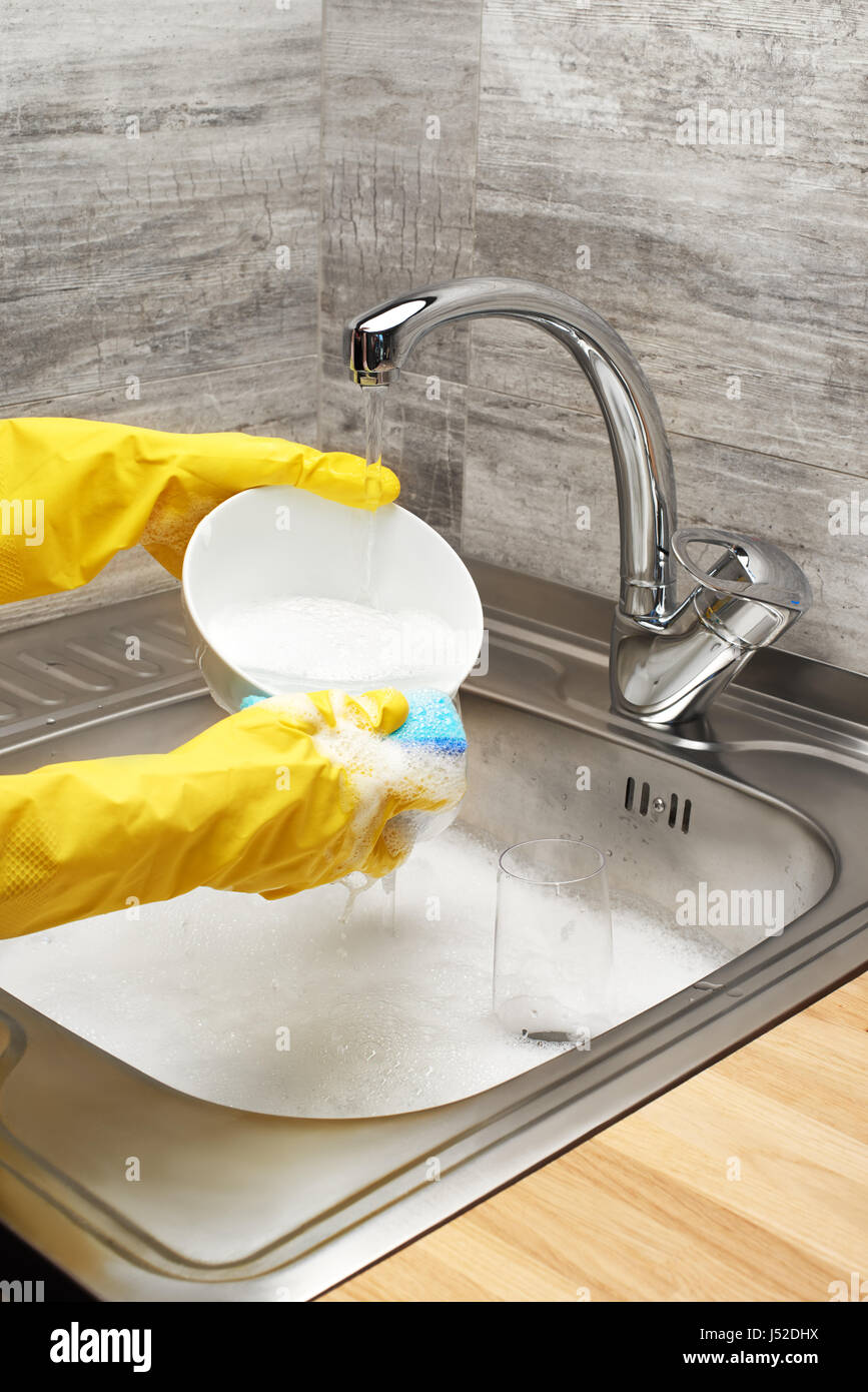 Nahaufnahme von weiblichen Händen Gummischutz Handschuhe waschen Schüssel weiß mit blauen Reinigung gegen Küchenspüle voller Schaum und b. sponge gelb Stockfoto