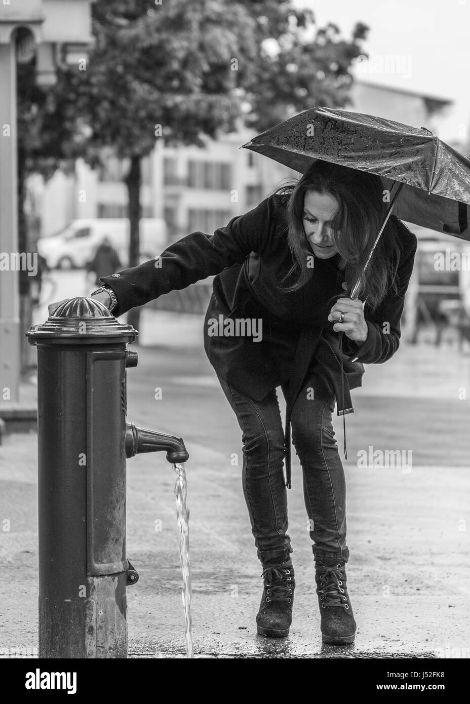 Ein Regentag in Annecy in Schwarz und Weiß ein weibliches Model mit einem Regenschirm von einem Brunnen Stockfoto