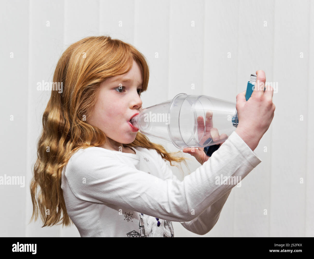 Ein sieben Jahre altes Mädchen mit einer Ventolin-Inhalator mit einem Spacer volumatic Gerät zur Linderung von Asthma. Stockfoto