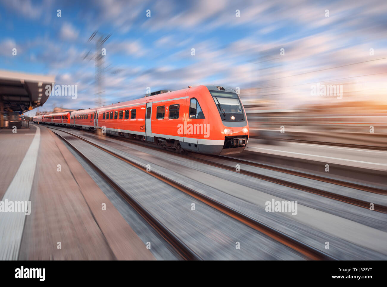 Rote moderne high-Speed-Zug in Bewegung am Bahngleis bei Sonnenuntergang in Europa. Zug am Bahnhof mit Motion blur Effekt. Industrielle Landschaft wi Stockfoto