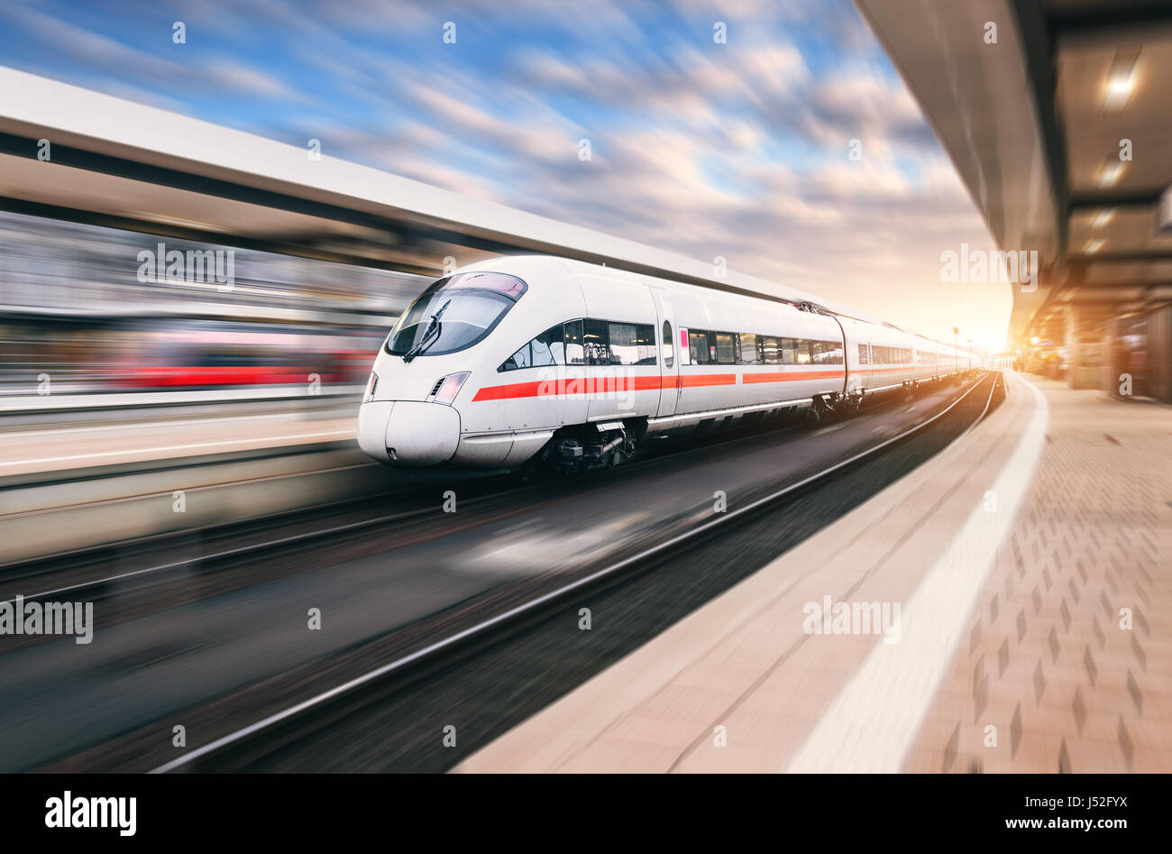 Weiße moderne high-Speed-Zug in Bewegung am Bahnhof bei Sonnenuntergang. Zug auf Bahngleis mit Motion blur Effekt in Europa Abend. Eisenbahn-pl Stockfoto