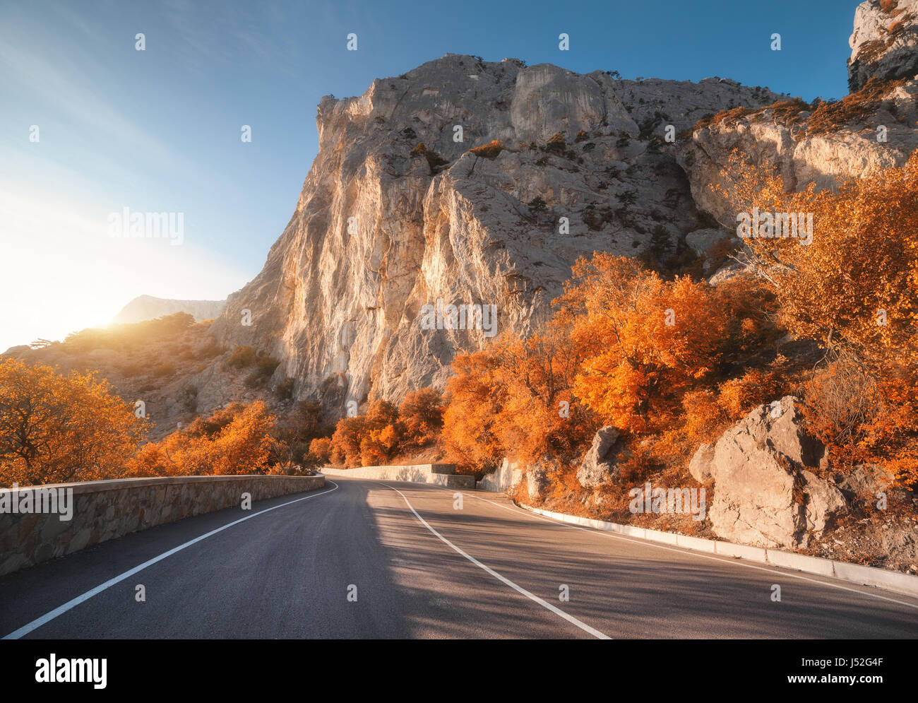 Asphaltierte Straße im Herbst bei Sonnenaufgang. Landschaft mit schönen leeren Bergstraße mit perfekter Asphalt, hohe Felsen, Bäumen und sonnigen Himmel. Jahrgang Stockfoto