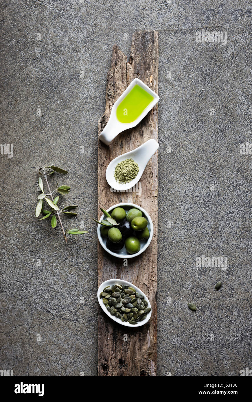 Grüne Lebensmittel: Macha Tee, Oliven, Olivenöl, Kürbiskernöl auf grauem Hintergrund Stockfoto