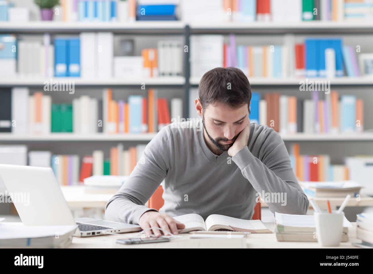 Young konzentrierte sich kluger Mann im Büro zu studieren und ein Buch lesen, Regale auf Hintergrund Stockfoto