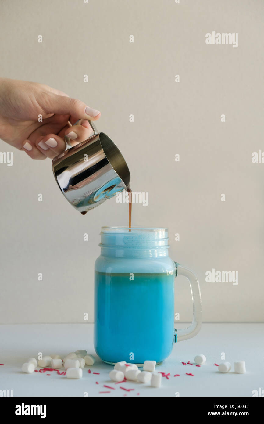 Frau ist Kaffee in stilisierten Einmachglas Tasse farbige blaue Milch gießen. Milch-Shake, Cocktaill, Frappuccino.  Einhorn Kaffee, Einhorngericht. Stockfoto